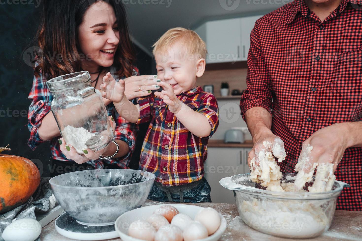 pai, mãe e filho pequeno cozinham uma torta foto