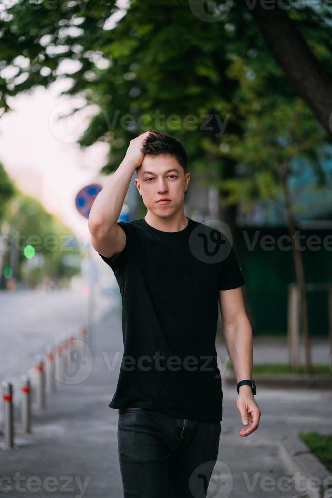 jovem adulto em uma camiseta preta e jeans caminha em uma rua da cidade foto