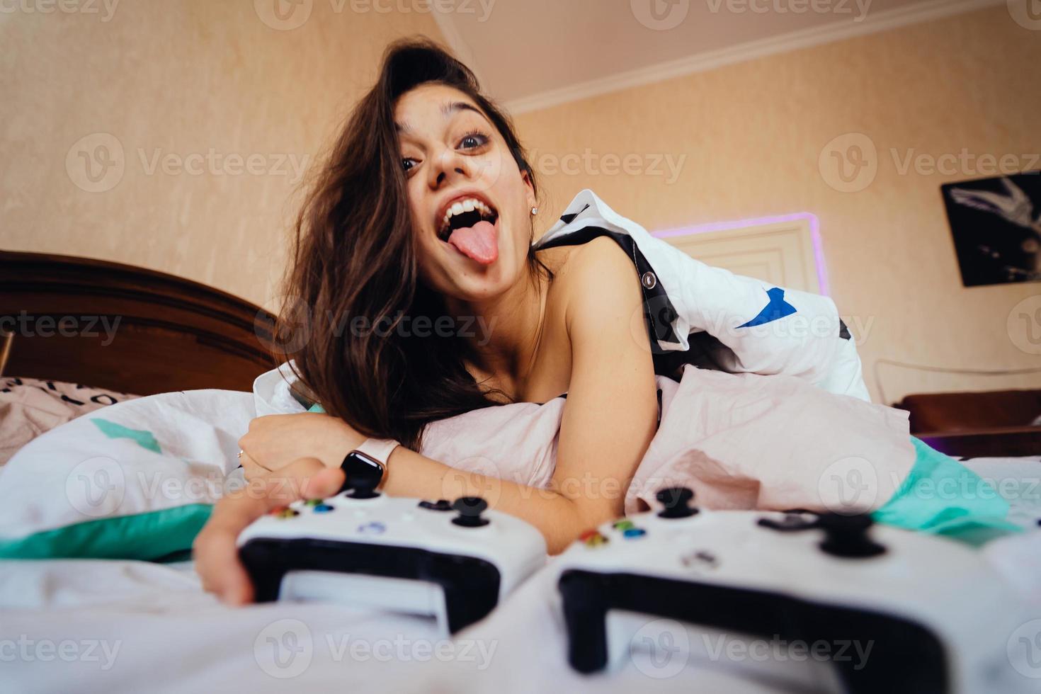 garota engraçada deitada na cama e jogando videogame, segurando o controlador foto