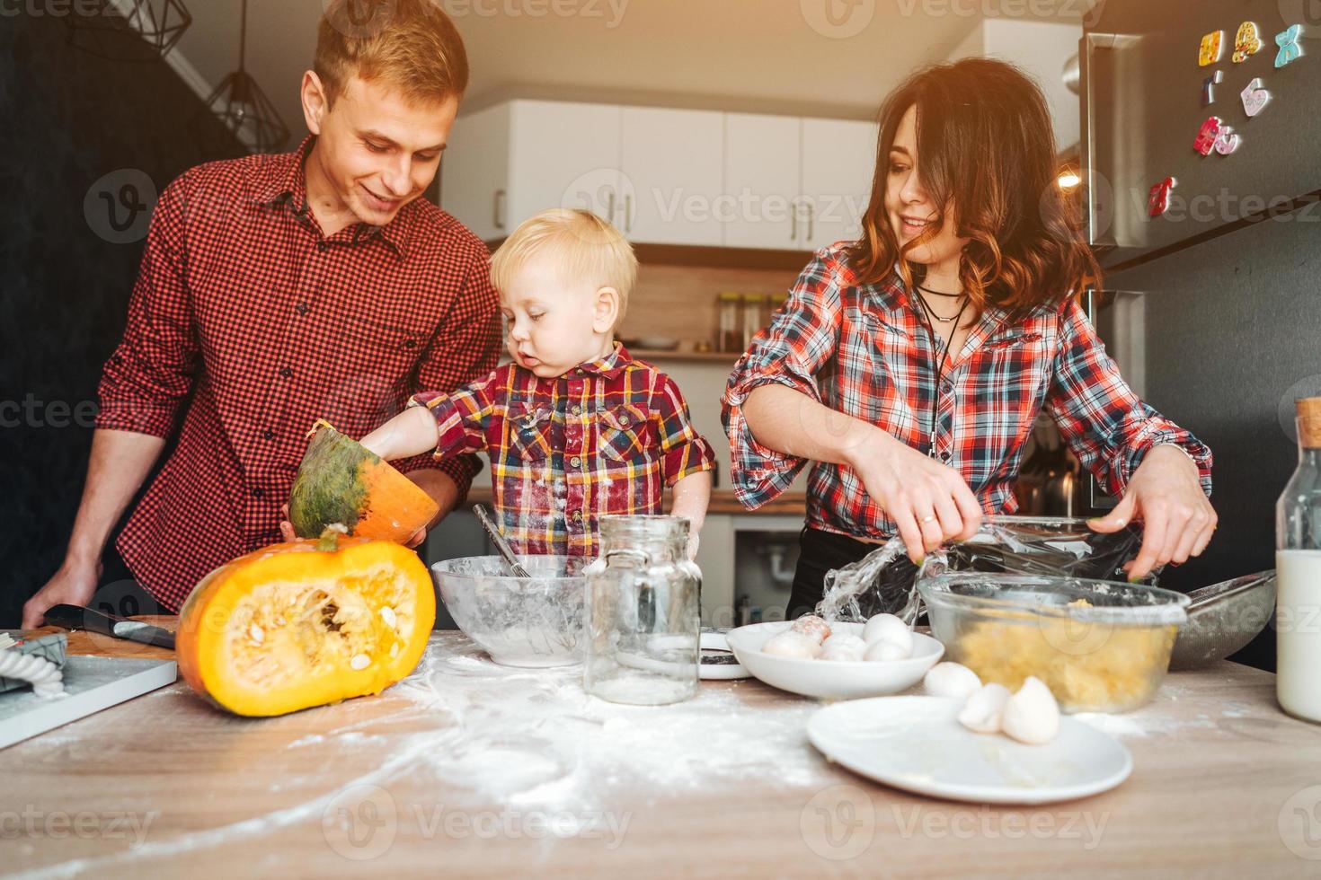 pai, mãe e filho pequeno cozinham uma torta foto