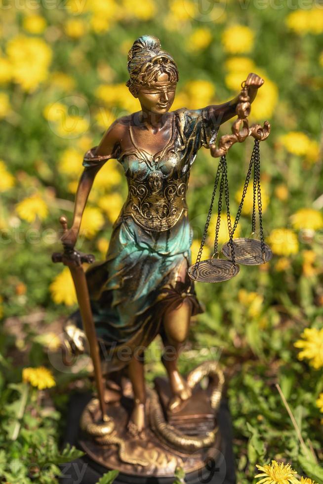 estátua de themis contra um gramado de dentes de leão. símbolo de justiça e lei, crime e punição. foto