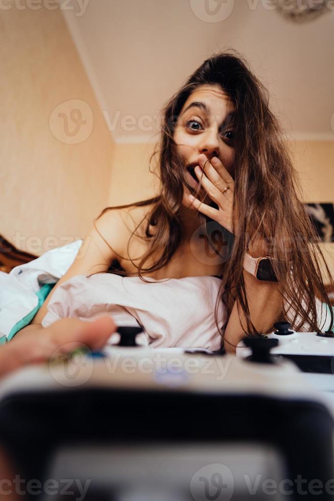 garota engraçada deitada na cama e jogando videogame, segurando o controlador foto