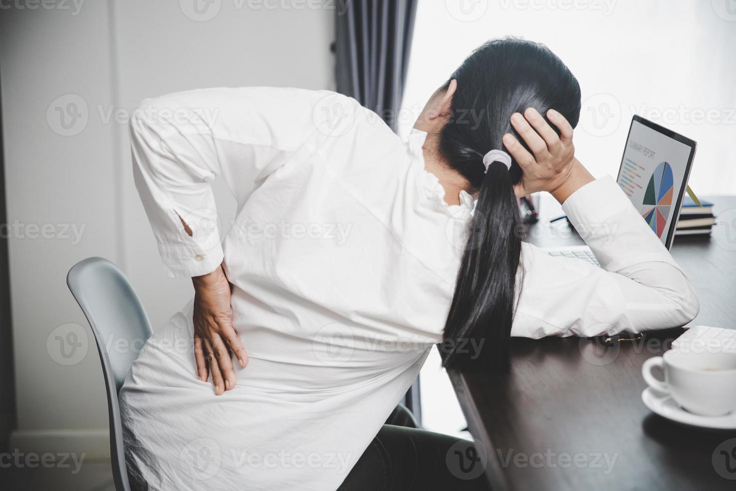 jovem mulher asiática está sentada no trabalho e tem dor de tensão no pescoço. síndrome do escritório conceito dor nas costas por doença ocupacional, mulher com dor muscular por usar computador portátil, dor nas costas. foto