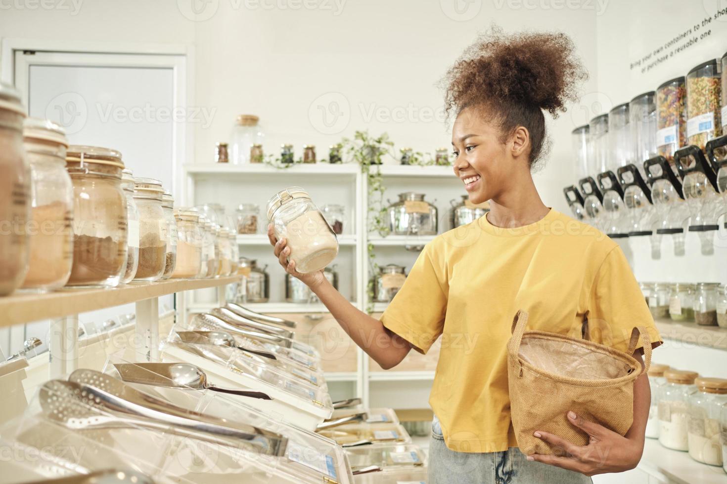 jovem mulher afro-americana está escolhendo e comprando produtos orgânicos na loja de recarga com saco reutilizável, mercearia com desperdício zero e estilos de vida sustentáveis, ecologicamente corretos e sem plástico. foto