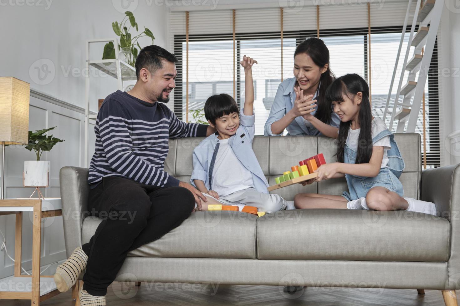 feliz asiático adorável tailandês cuidado familiar, pai, mãe e crianças pequenas se divertem brincando com blocos de brinquedos coloridos juntos no sofá na sala branca, fim de semana de lazer e estilo de vida de bem-estar doméstico. foto