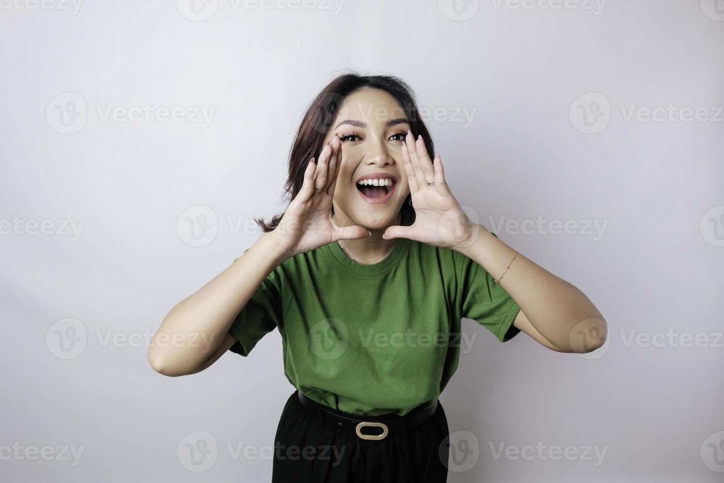 jovem mulher bonita vestindo uma camiseta verde gritando e gritando alto com a mão na boca dela. conceito de comunicação. foto