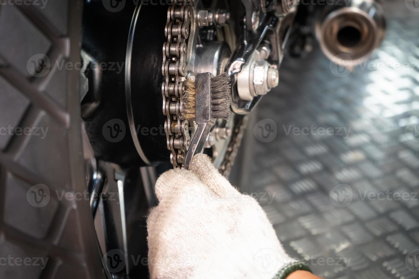 mecânico de motocicleta usando luvas usando escova de arame para limpar a roda dentada traseira da motocicleta na garagem de motos, conceito de manutenção e reparo da motocicleta, foto