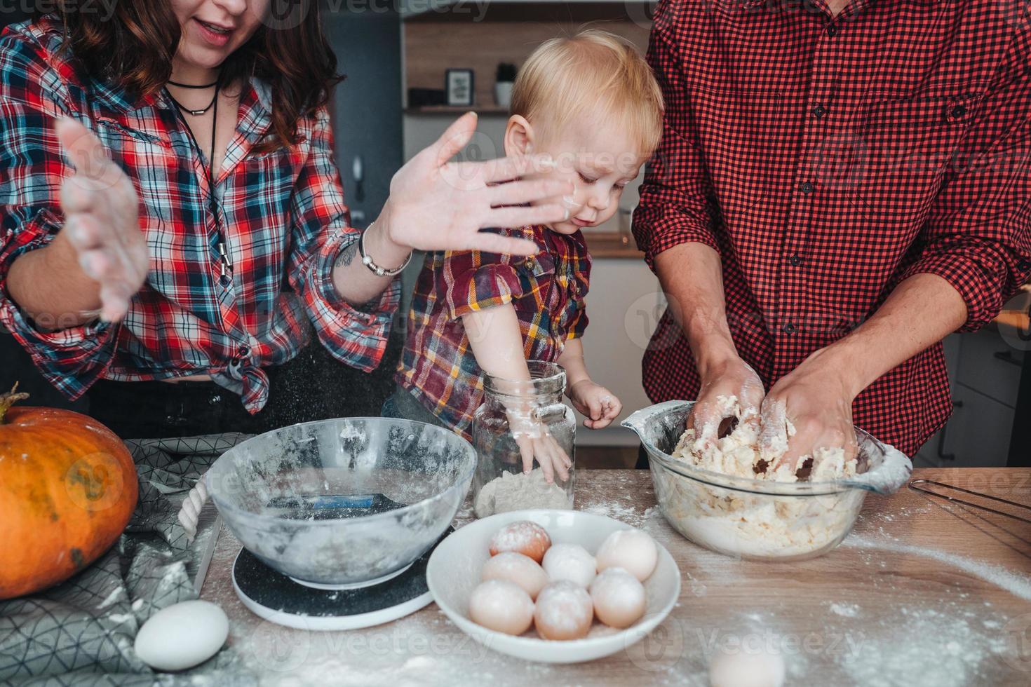 pai, mãe e filho pequeno cozinham uma torta foto