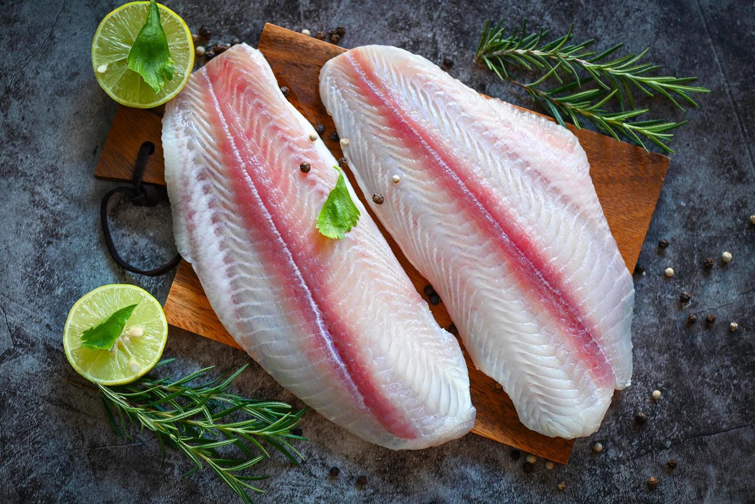 filé de peixe pangasius cru fresco com ervas e especiarias pimenta preta limão limão, filé de peixe na placa de madeira com ingredientes para cozinhar, carne dolly peixe tilápia listrado bagre foto