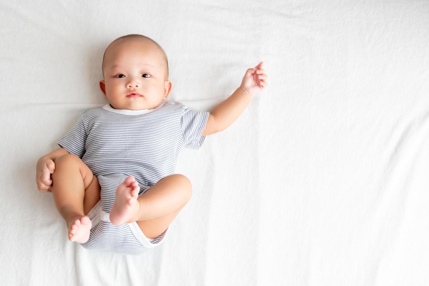 bebê de vista superior vestindo uma camisa listrada, levantando os braços e as pernas em um tapete branco. foto