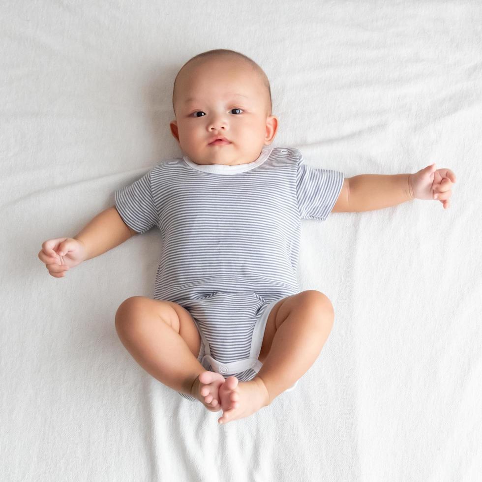 vista superior é um menino vestindo uma camisa listrada. deite-se com as pernas para cima e os braços estendidos na cama. foto