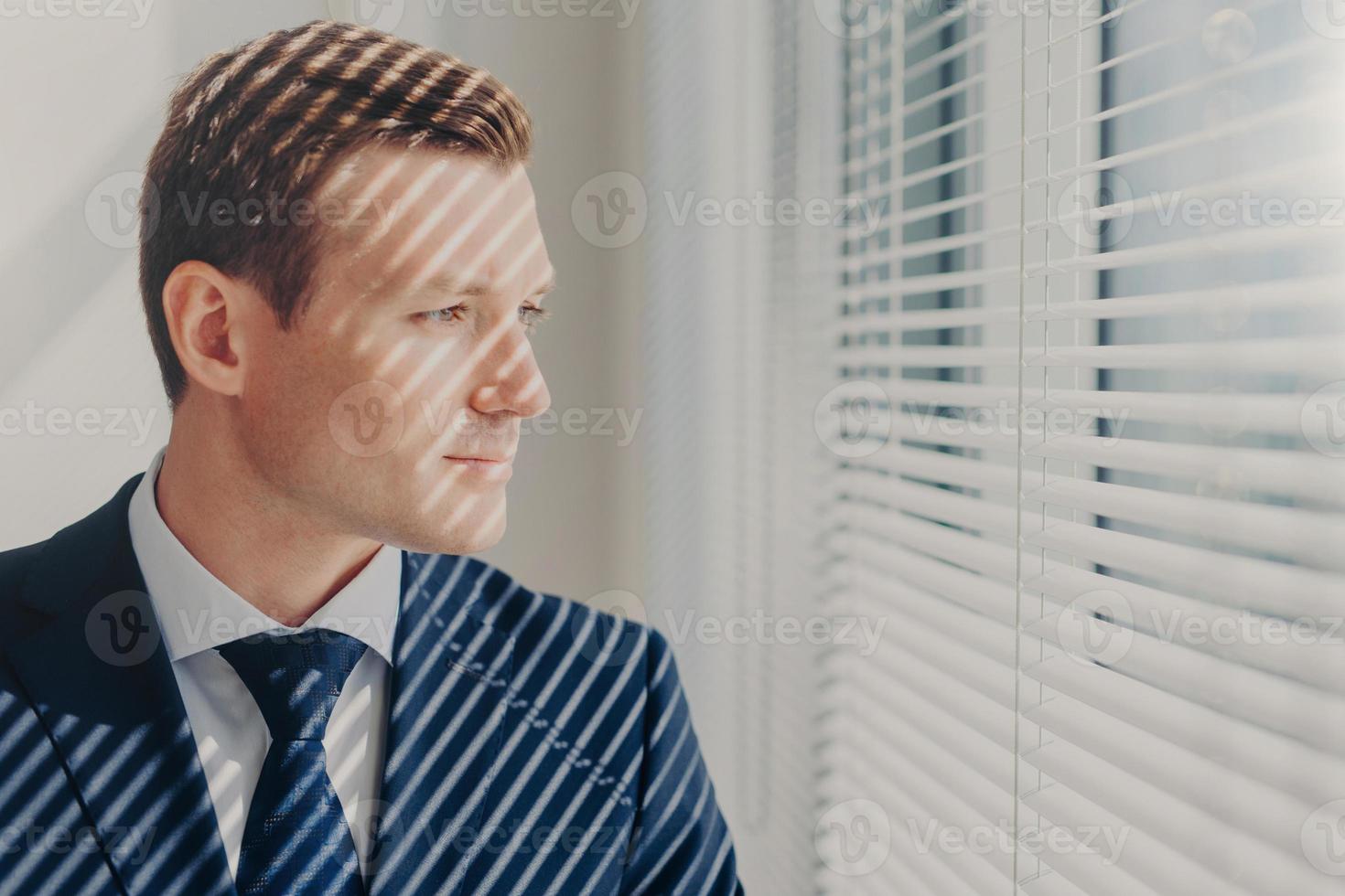 pessoas e conceito de carreira. jovem empresário de terno rico, pensa no futuro de sua empresa, fica perto da janela do escritório, concentrou um olhar pensativo. diretor administrativo masculino interno no gabinete foto