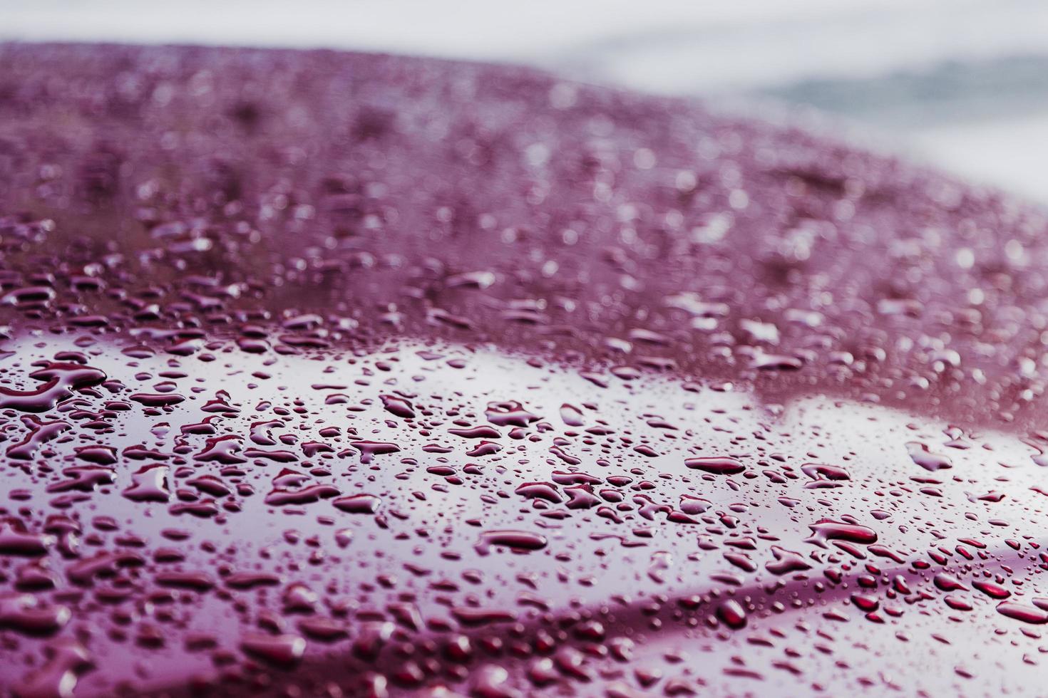 superfície molhada com gotas de água após o tempo chuvoso. backround vermelho coberto com respingos de água. pequenas gotas, textura. tiro horizontal. gota de água no painel metálico do veículo. foto