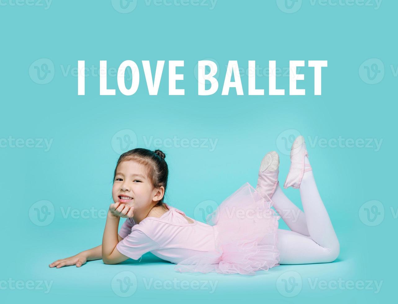 linda garotinha asiática sorridente em um terno rosa está dançando balé na escola, espaço vazio em estúdio tiro isolado em fundo azul colorido foto