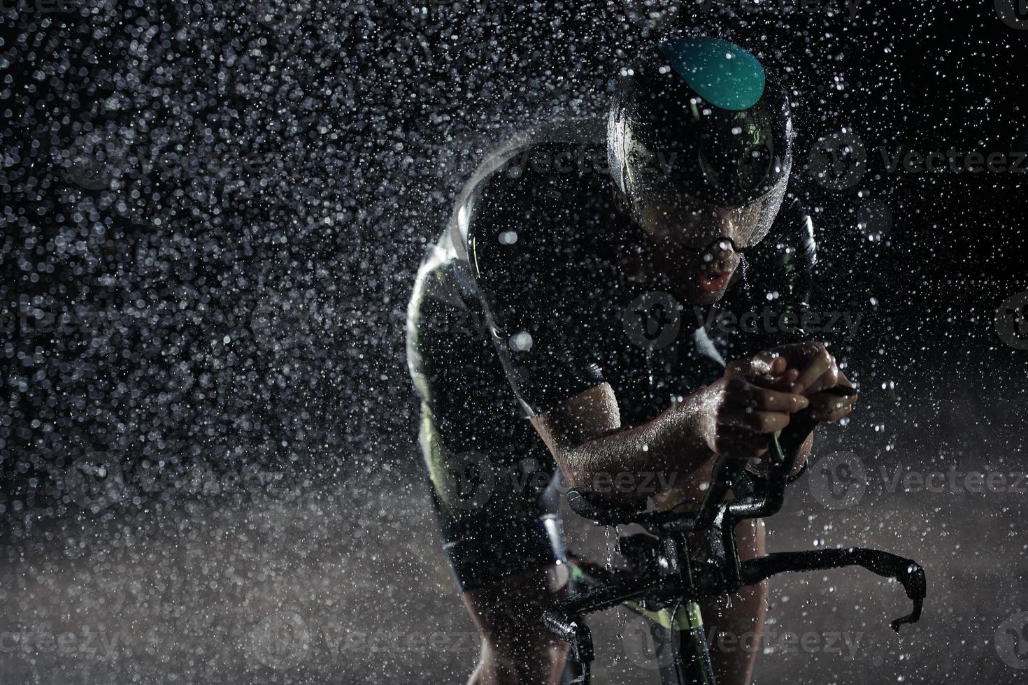 atleta de triatlo andando de bicicleta rápido na noite chuvosa foto