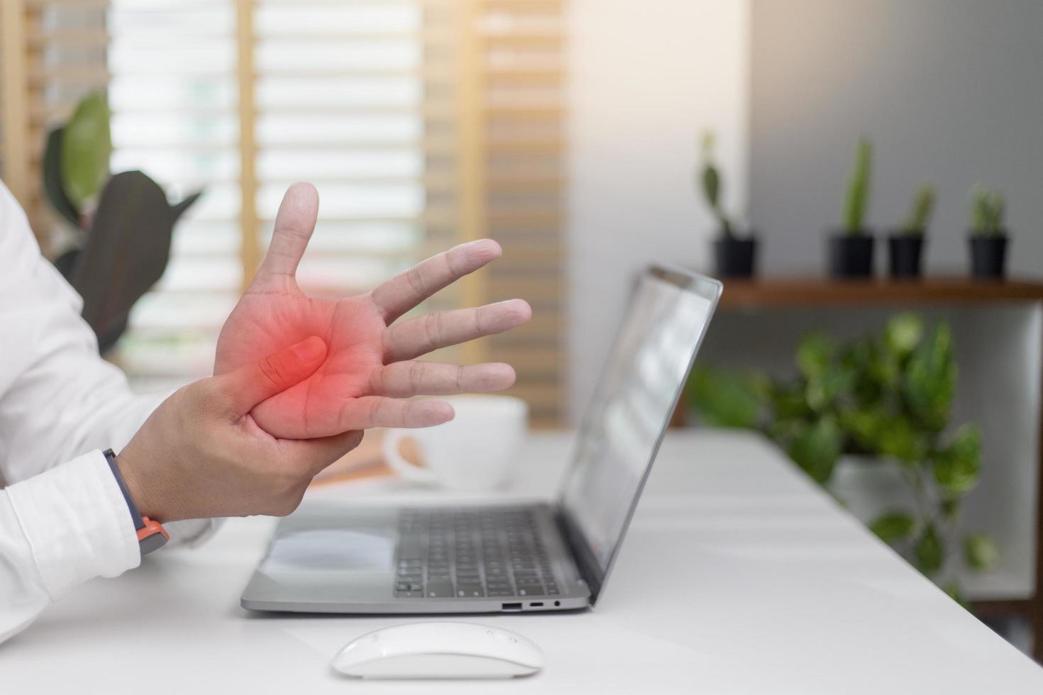 trabalhador do sexo masculino sentado no escritório com um laptop dolorido massagem na palma da mão compressão do nervo músculos tensos comichão nas mãos depois de digitar em um laptop foto