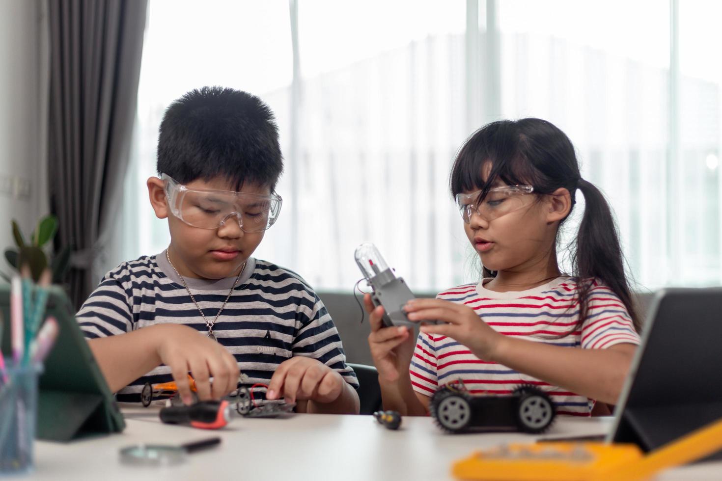 duas crianças asiáticas se divertindo aprendendo codificação juntas, aprendendo remotamente em casa, ciência da haste, educação escolar em casa, distanciamento social divertido, isolamento, novo conceito normal foto