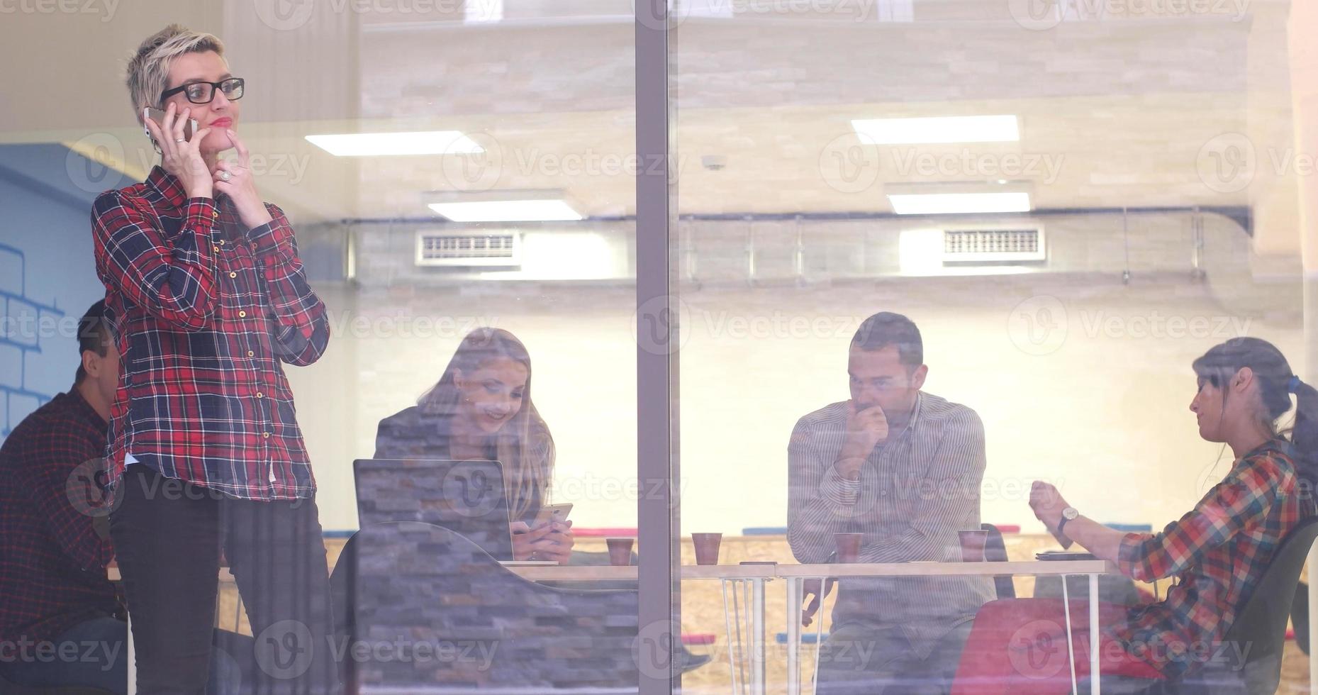 mulher de negócios olhando pela janela e usando um telefone celular durante a reunião de negócios foto
