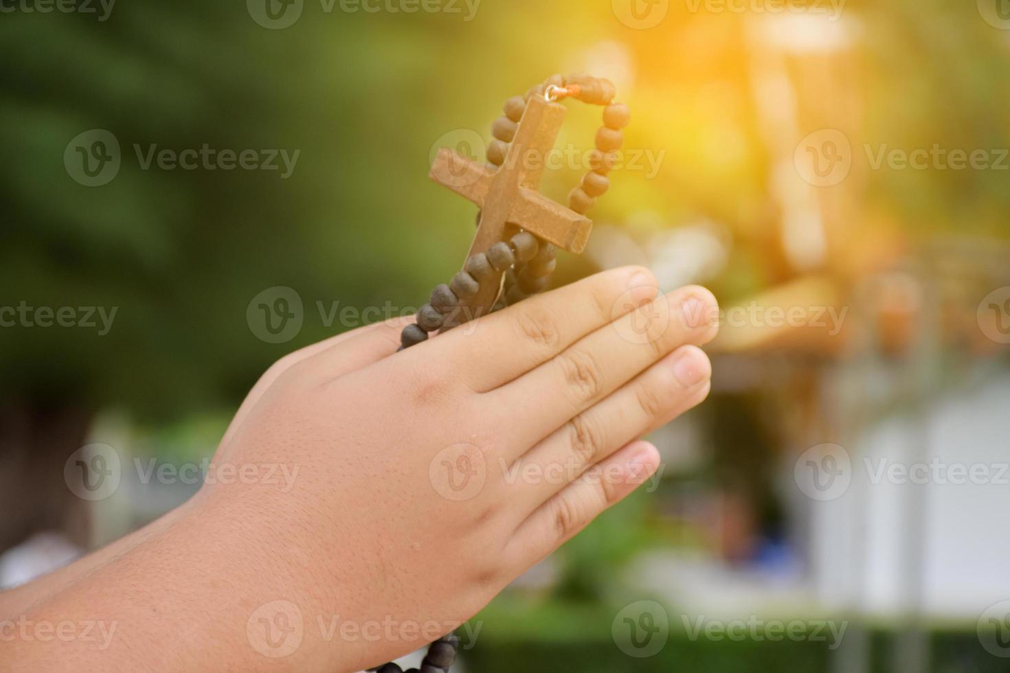 cruz de madeira e rosário de madeira são mantidos nas mãos da jovem oração católica asiática enquanto reza na área do parque do templo. foto