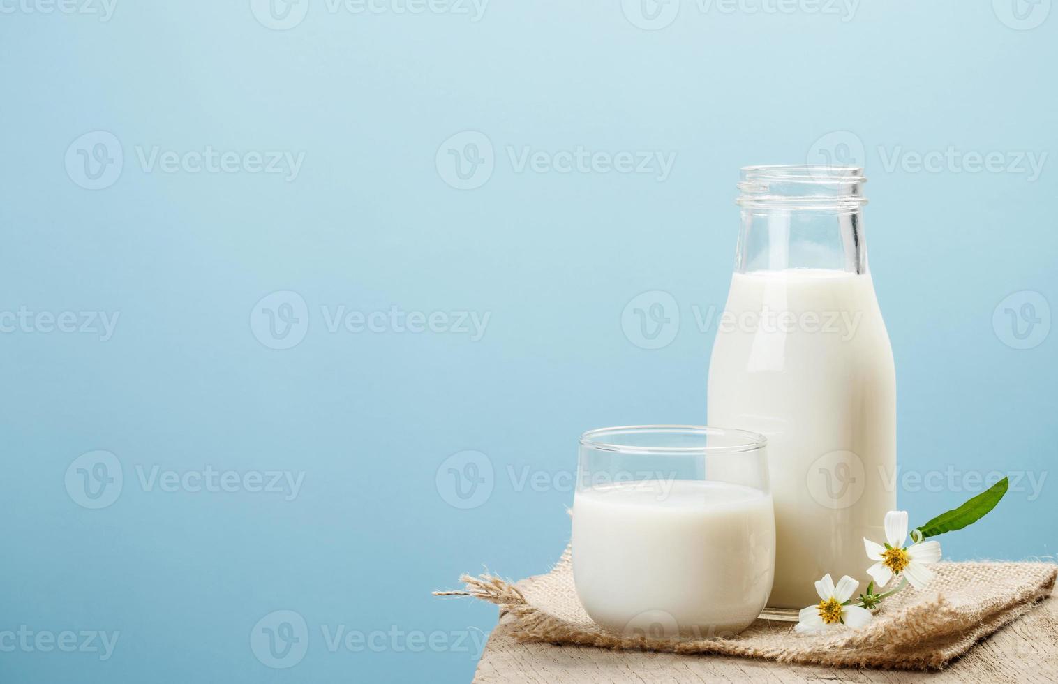 uma garrafa de leite e um copo de leite em uma mesa de madeira em um fundo azul, produtos lácteos saborosos, nutritivos e saudáveis foto