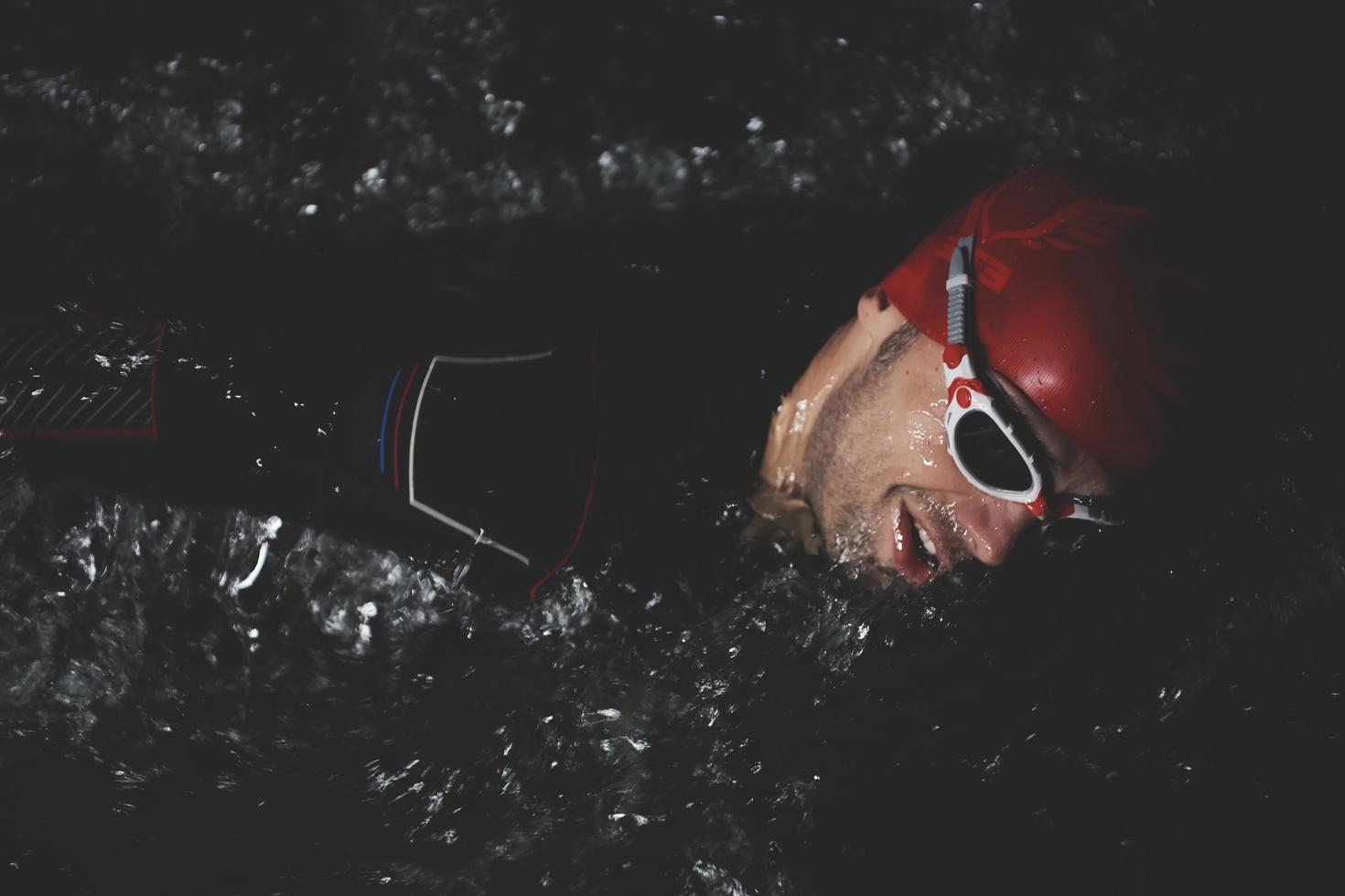 atleta de triatlo nadando na noite escura vestindo roupa de mergulho foto