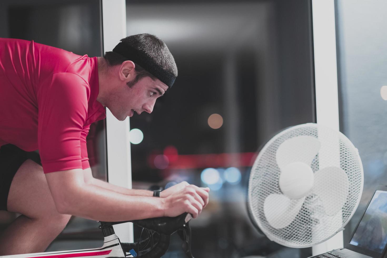 homem andando de bicicleta no treinador de máquina ele está se exercitando em casa à noite jogando jogo de corrida de bicicleta online foto