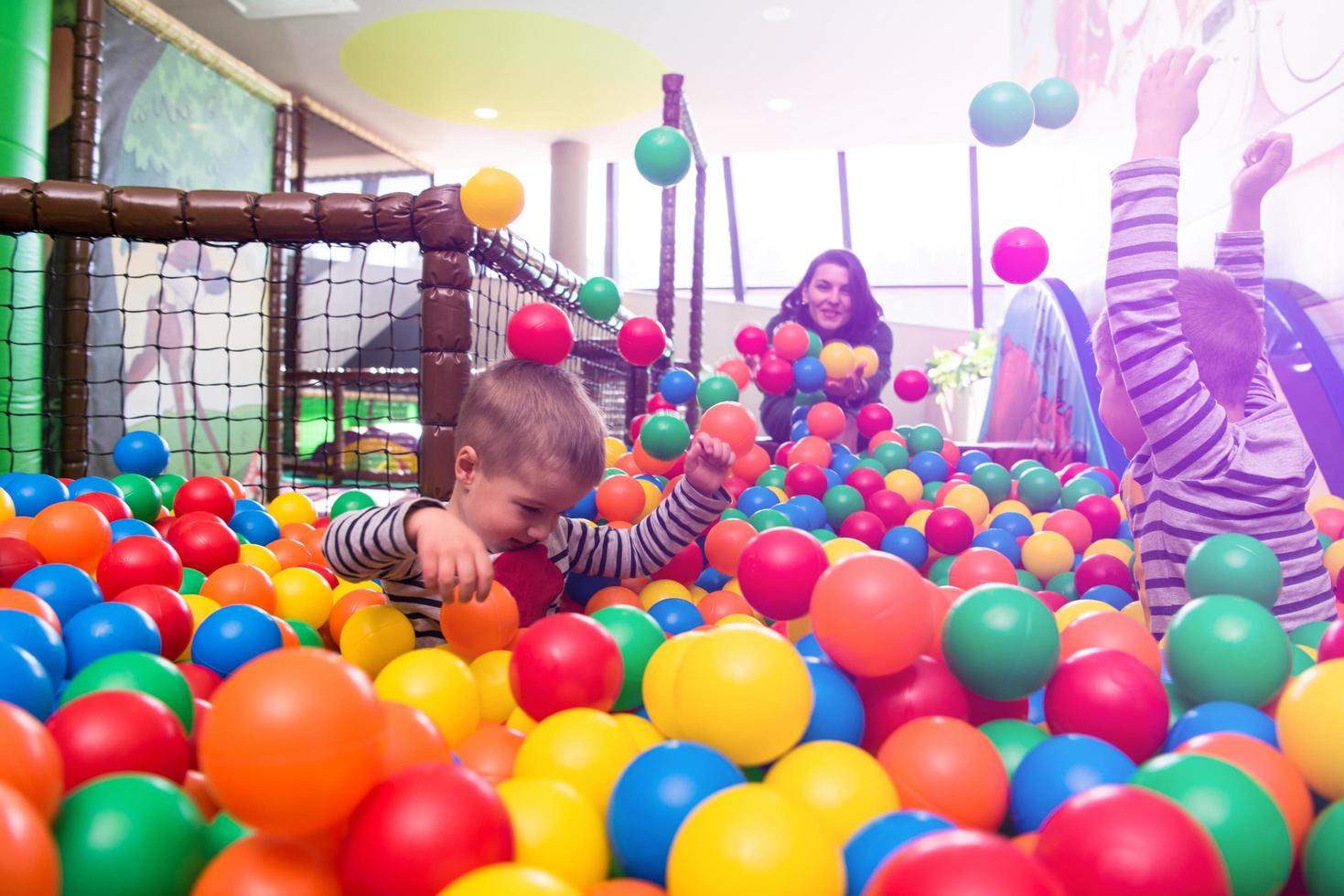 jovem mãe brincando com crianças na piscina com bolas coloridas foto