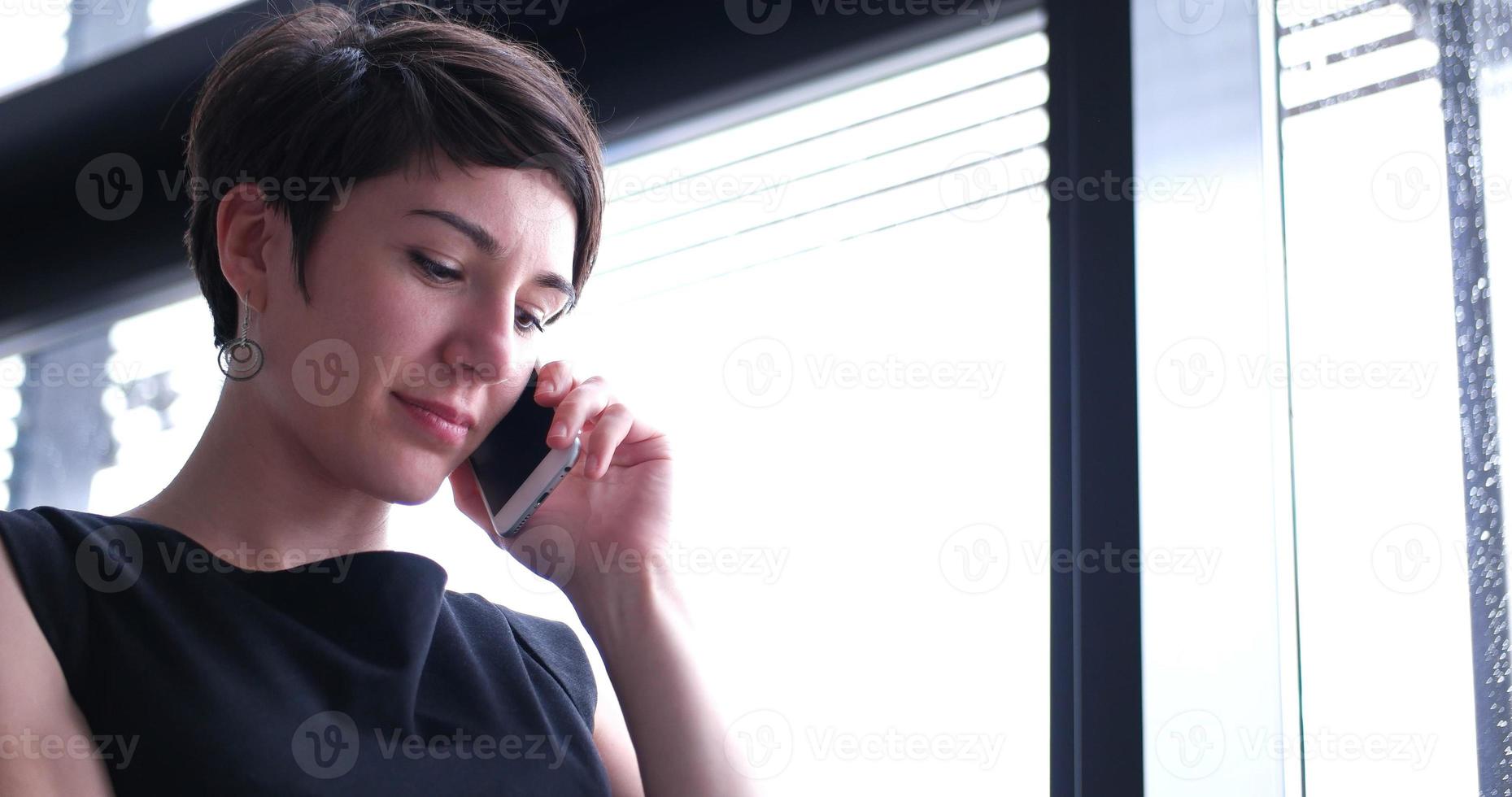 garota de negócios em um prédio moderno perto da janela com telefone foto