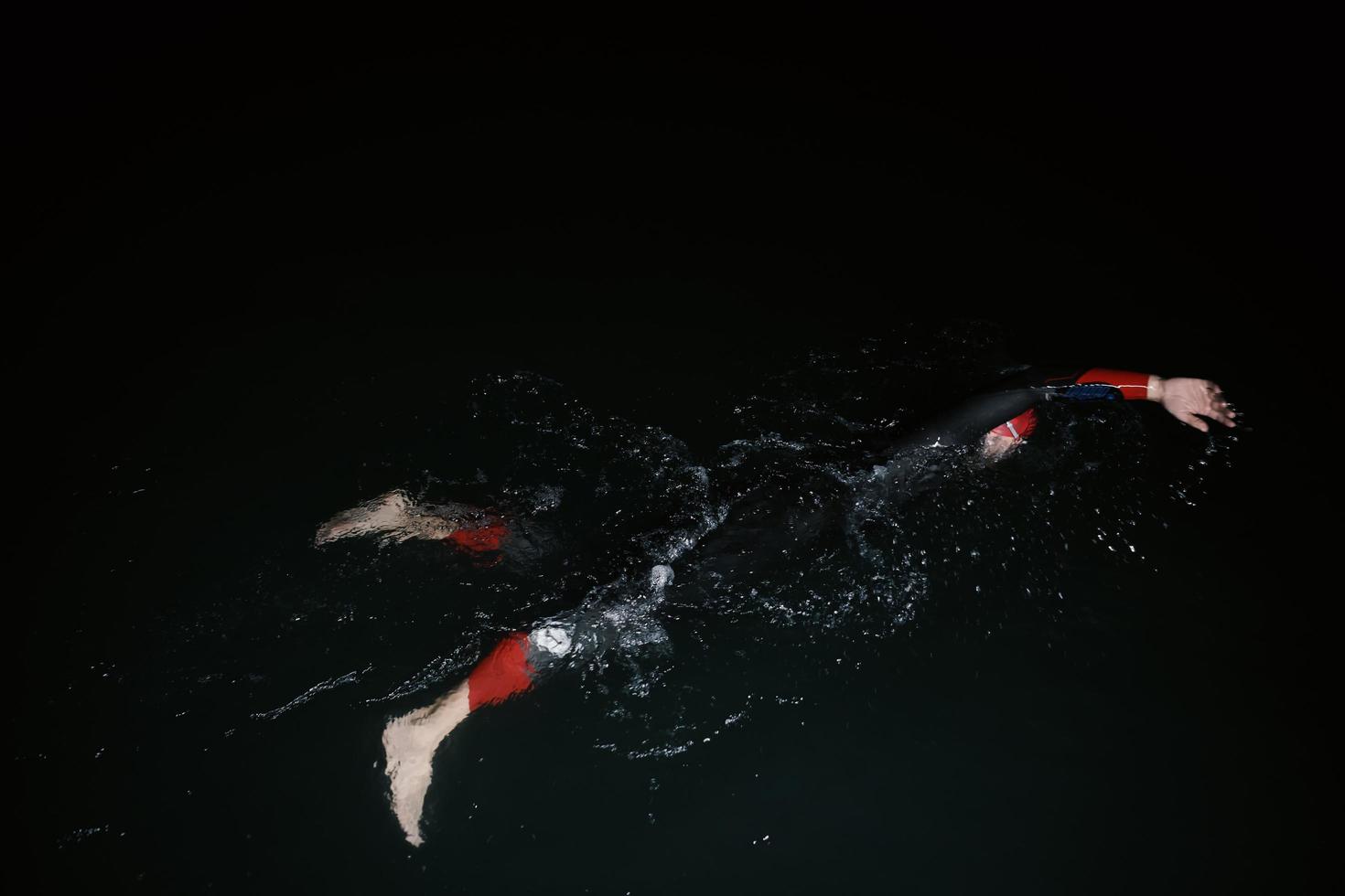 atleta de triatlo nadando na noite escura vestindo roupa de mergulho foto