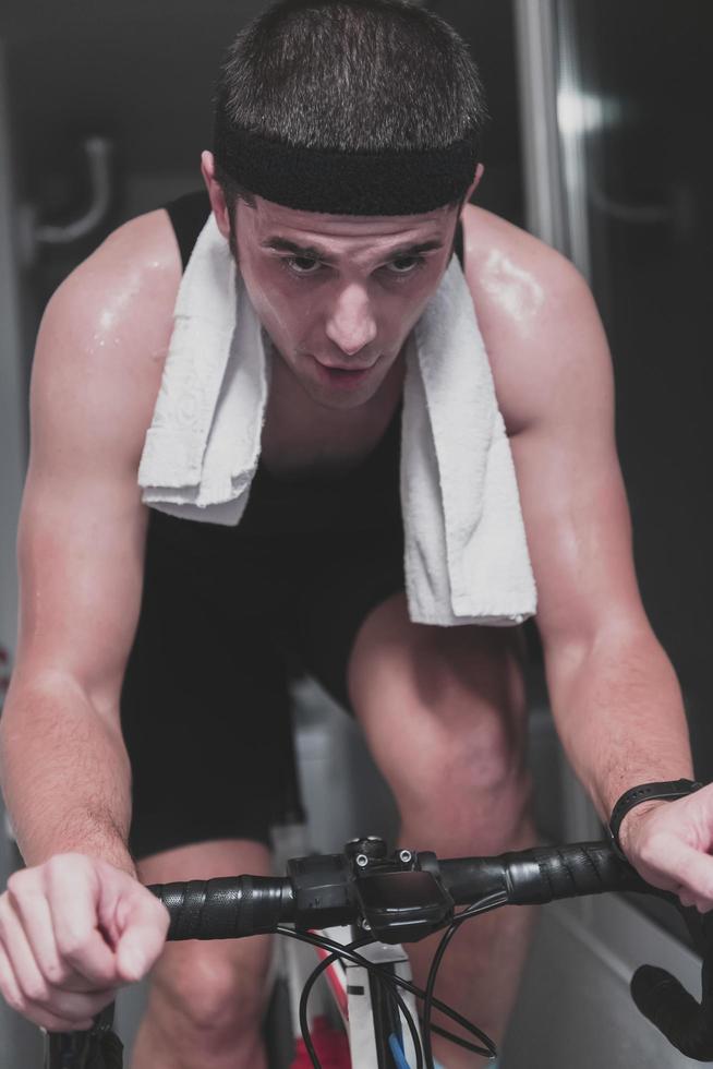 homem andando de bicicleta no treinador de máquina ele está se exercitando em casa à noite jogando jogo de corrida de bicicleta online foto