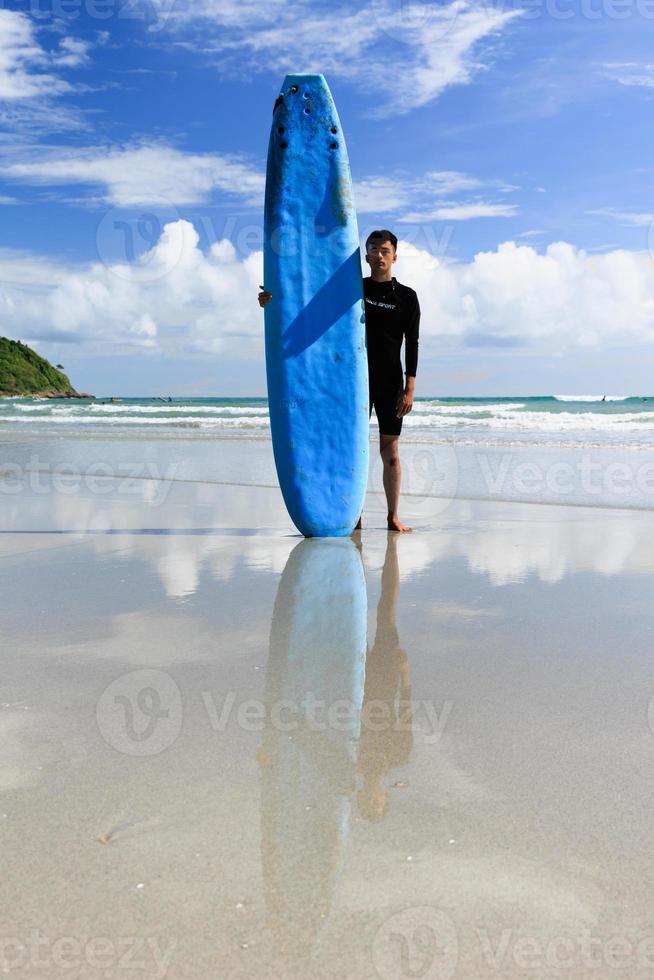 um jovem adolescente asiático em pé com autoconfiança segurando uma prancha macia pronta para esportes radicais surfando em férias na praia. foto