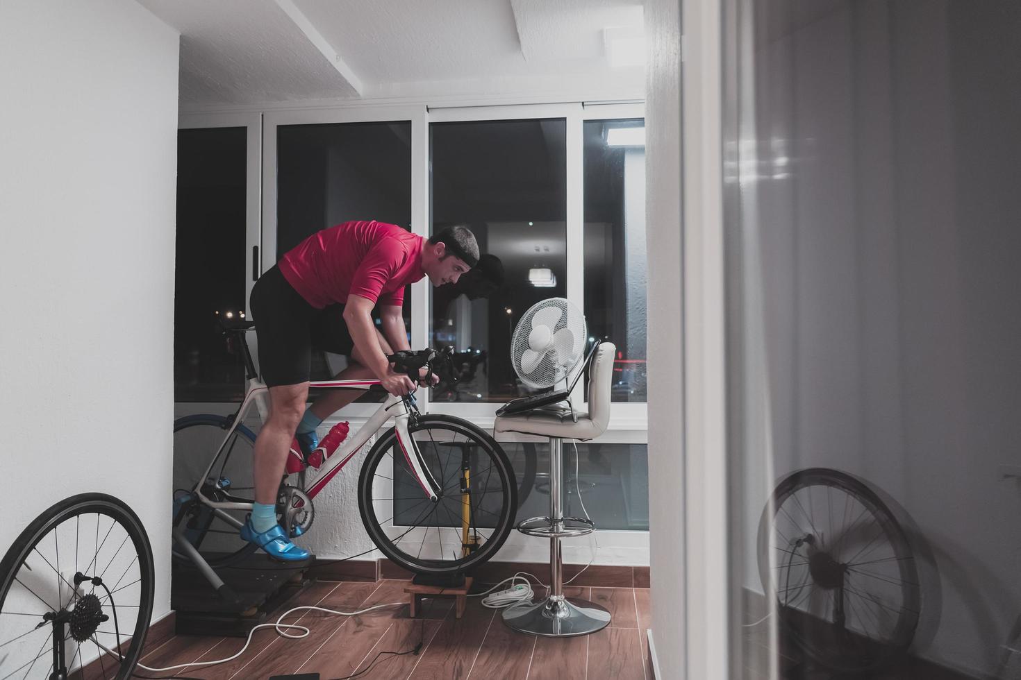 homem andando de bicicleta no treinador de máquina ele está se exercitando em casa à noite jogando jogo de corrida de bicicleta online foto