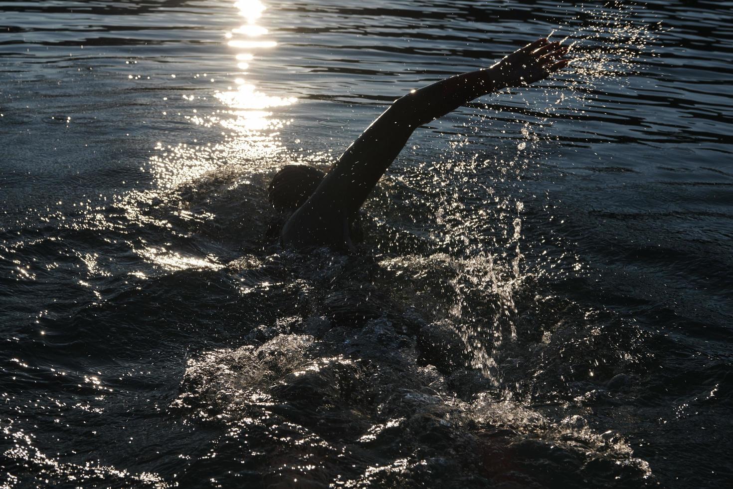 atleta de triatlo nadando no lago ao nascer do sol vestindo roupa de mergulho foto