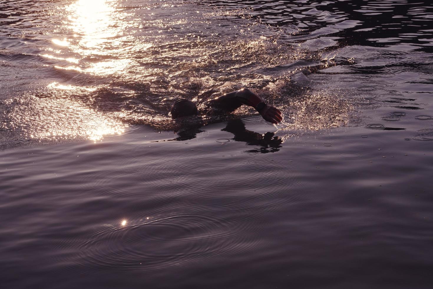 atleta de triatlo nadando no lago ao nascer do sol vestindo roupa de mergulho foto