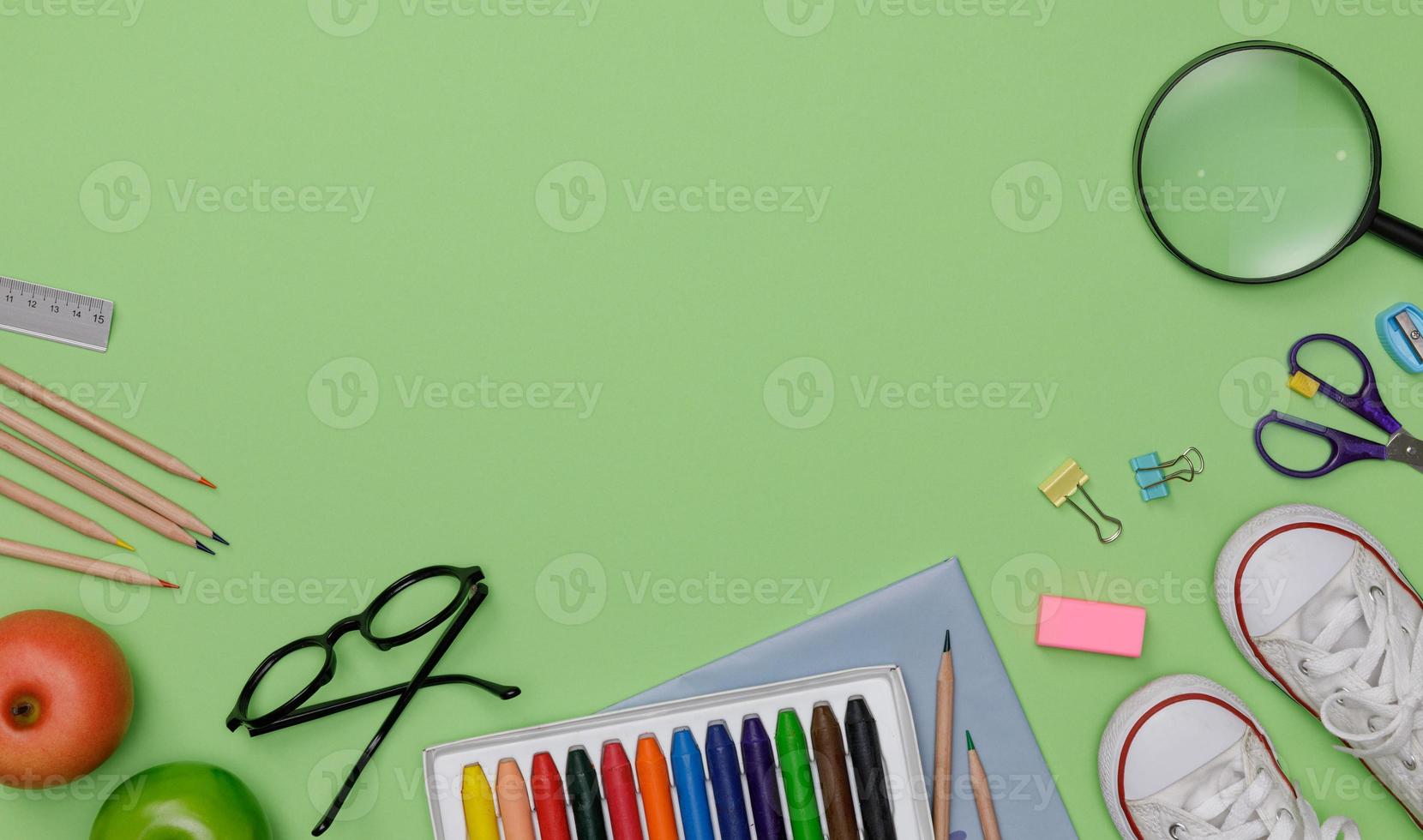 flatlay criativo de mesa verde de educação com livros de estudante, sapatos, giz de cera colorido, óculos, espaço vazio isolado em fundo verde, conceito de educação e volta às aulas foto