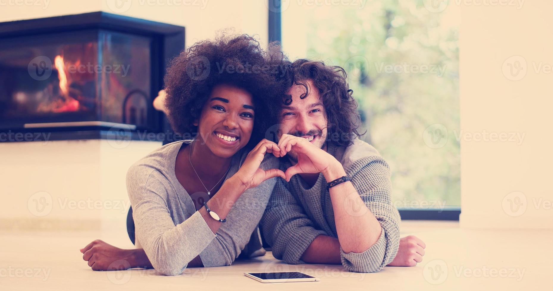 casal multiétnico mostrando um coração com as mãos no chão foto