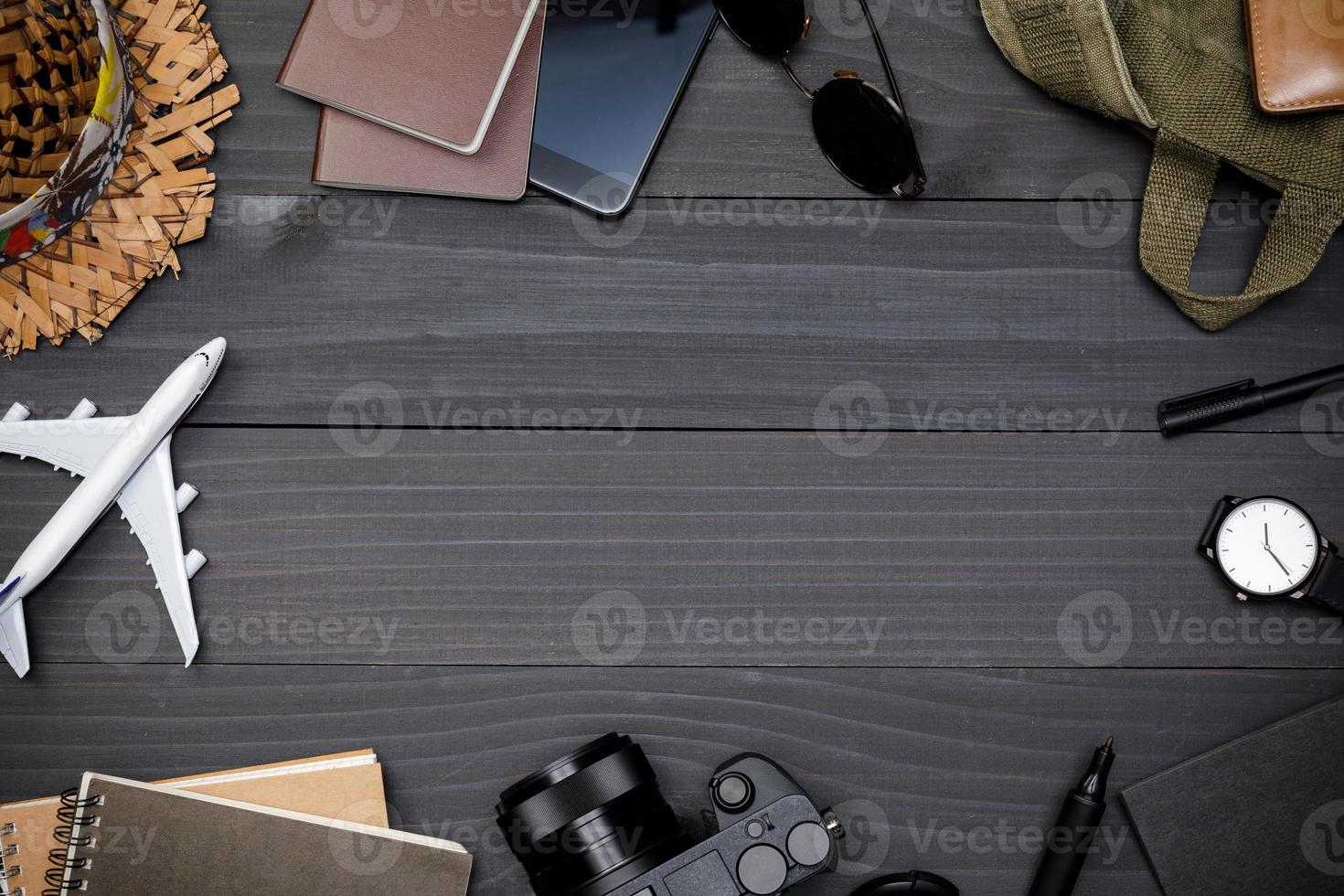 acessórios do viajante com passaporte, livros de plano de viagem, carteira, câmera, chapéu, mochila e brinquedo de avião na mesa de madeira preta, postura plana com espaço de cópia, plano de fundo do conceito de viagem foto