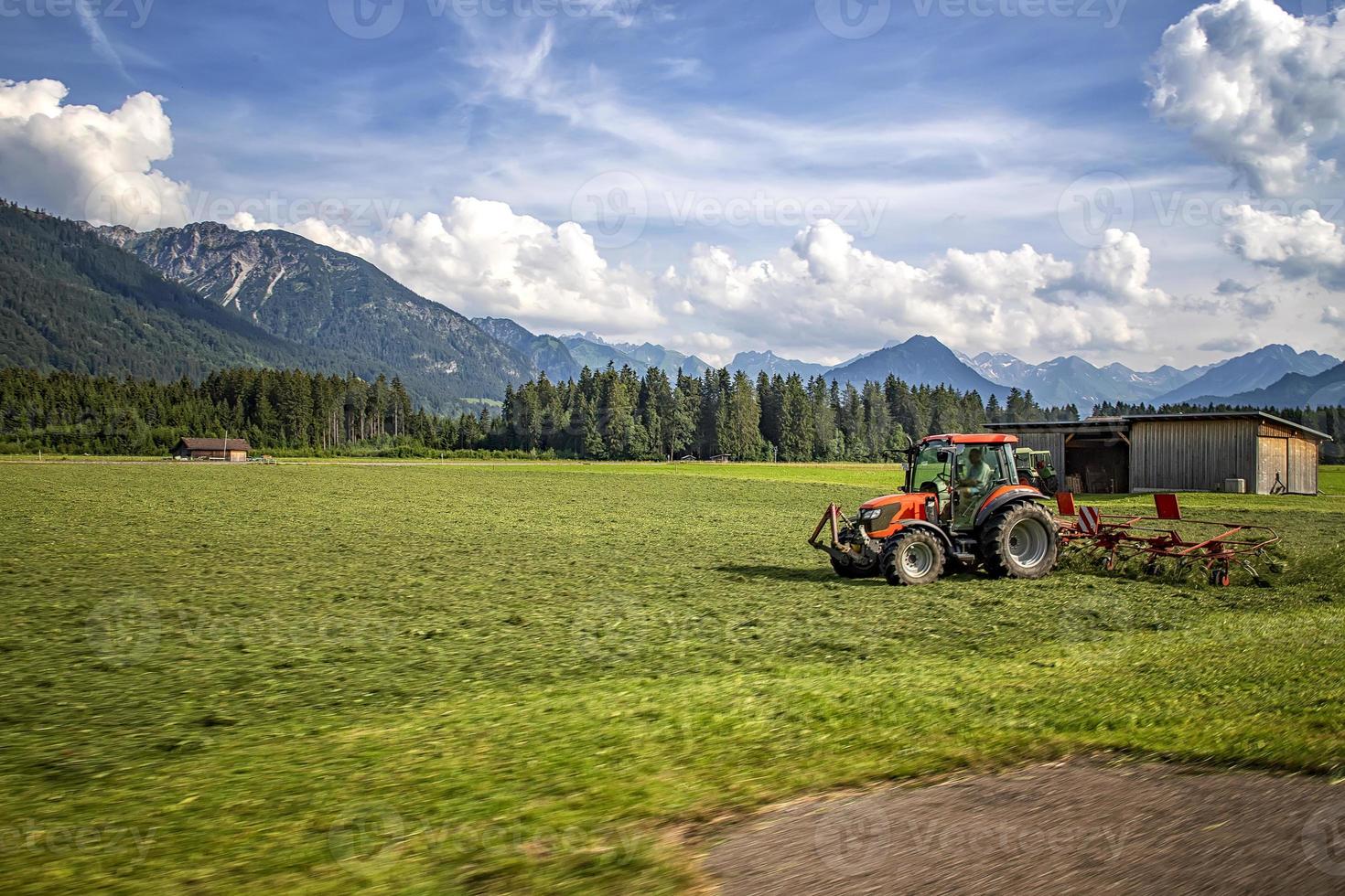 máquinas agrícolas, um trator coletando grama em um campo contra um céu azul. colheita da temporada, grama, terras agrícolas. foco seletivo foto