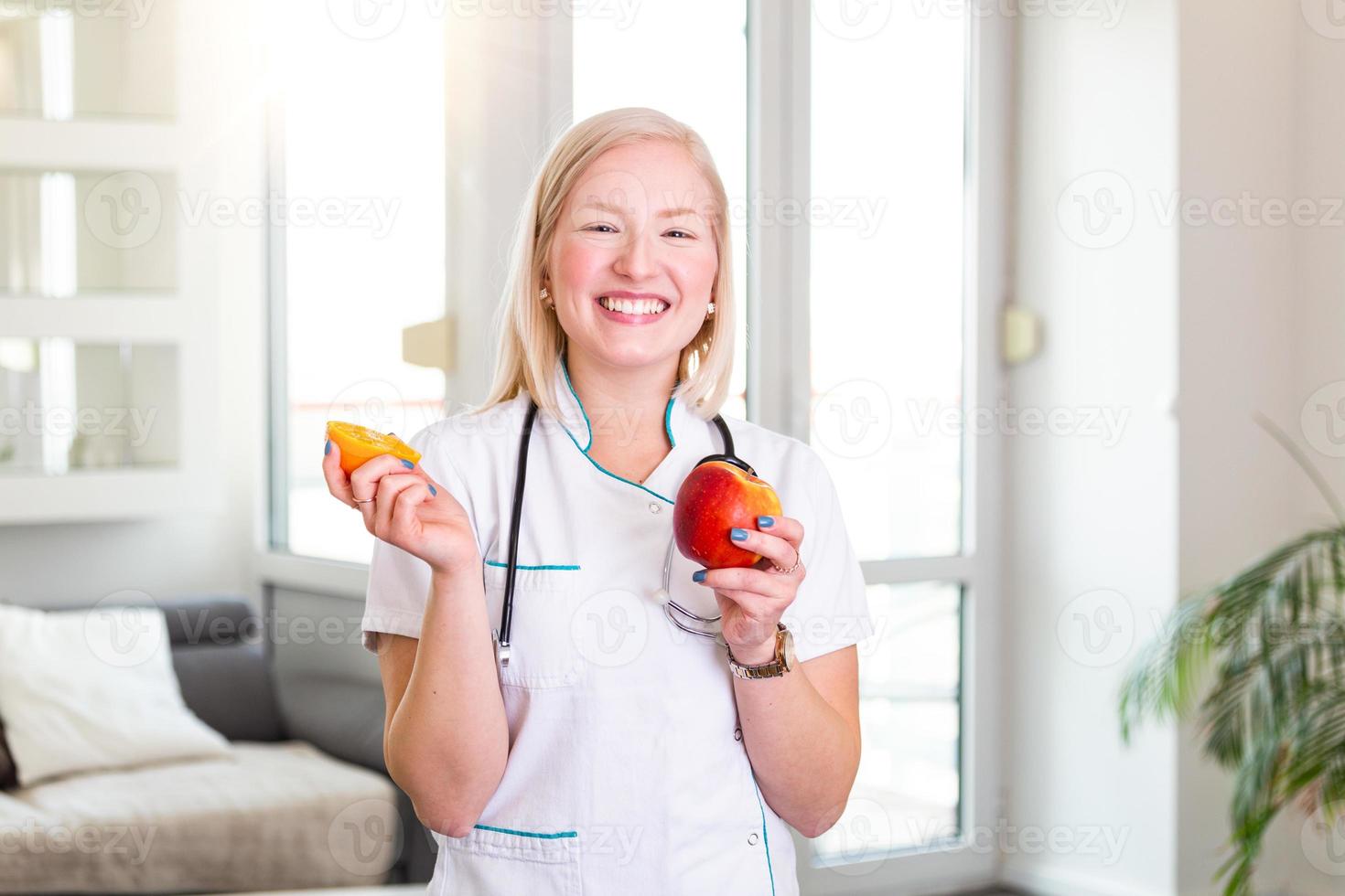 nutricionista sorridente em seu escritório, ela está segurando uma fruta e mostrando vegetais e frutas saudáveis, conceito de saúde e dieta. nutricionista feminina com frutas foto