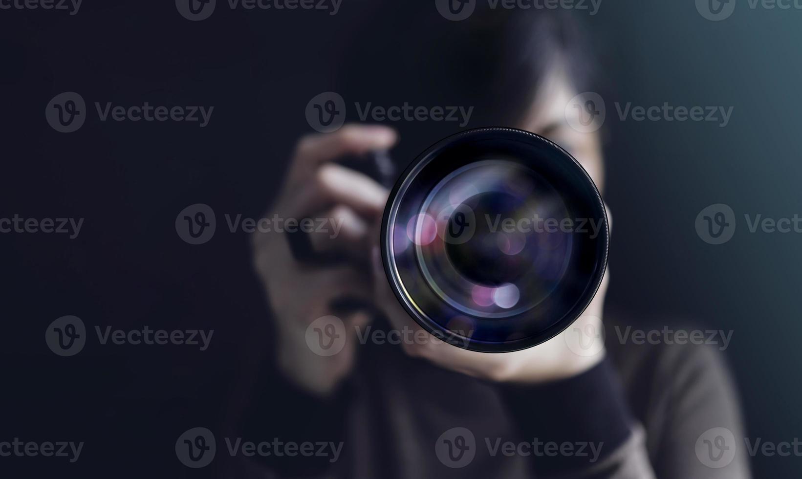fotógrafo tirando auto-retrato. mulher usando a câmera para tirar foto. tom escuro, vista frontal. foco seletivo na lente. direto para uma câmera foto