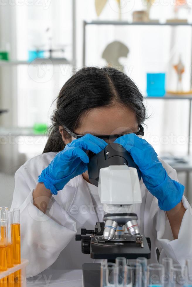 retrato de jovem aisan aprendendo ciências e olhando no microscópio em laboratório foto