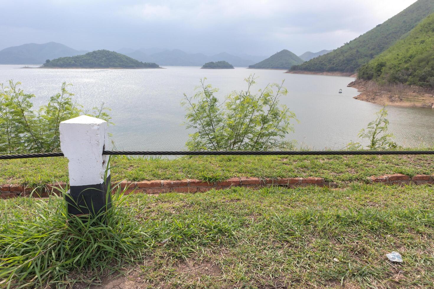 postes de concreto com cabos na estrada lateral com montanhas, rio e céu ao fundo foto