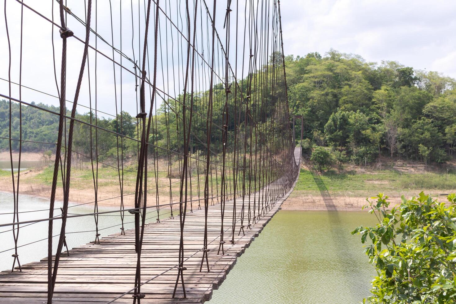 ponte suspensa no rio com montanhas e céu ao fundo foto