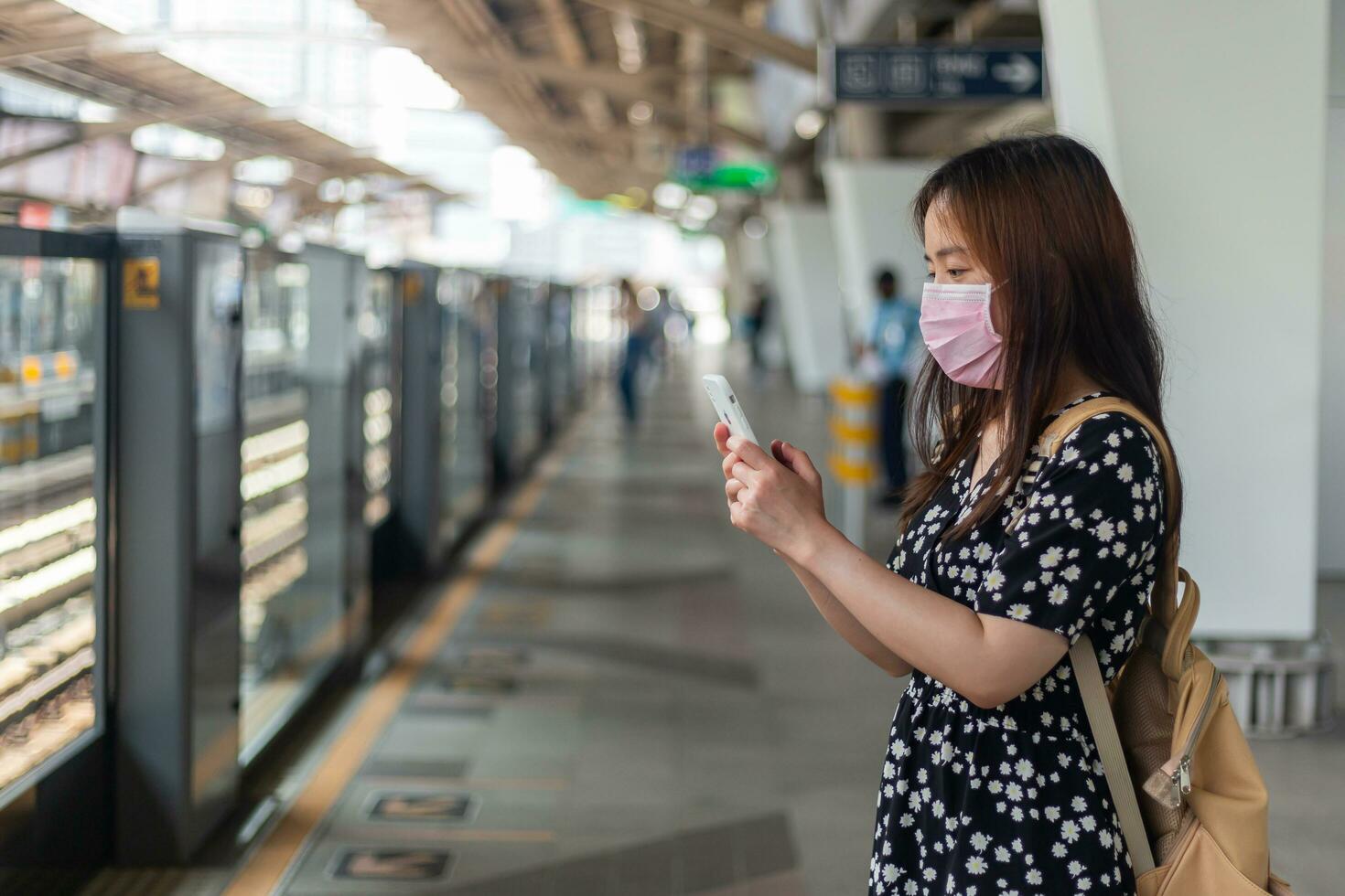 jovem mulher asiática passageira esperando trem do metrô quando digita telefone celular foto