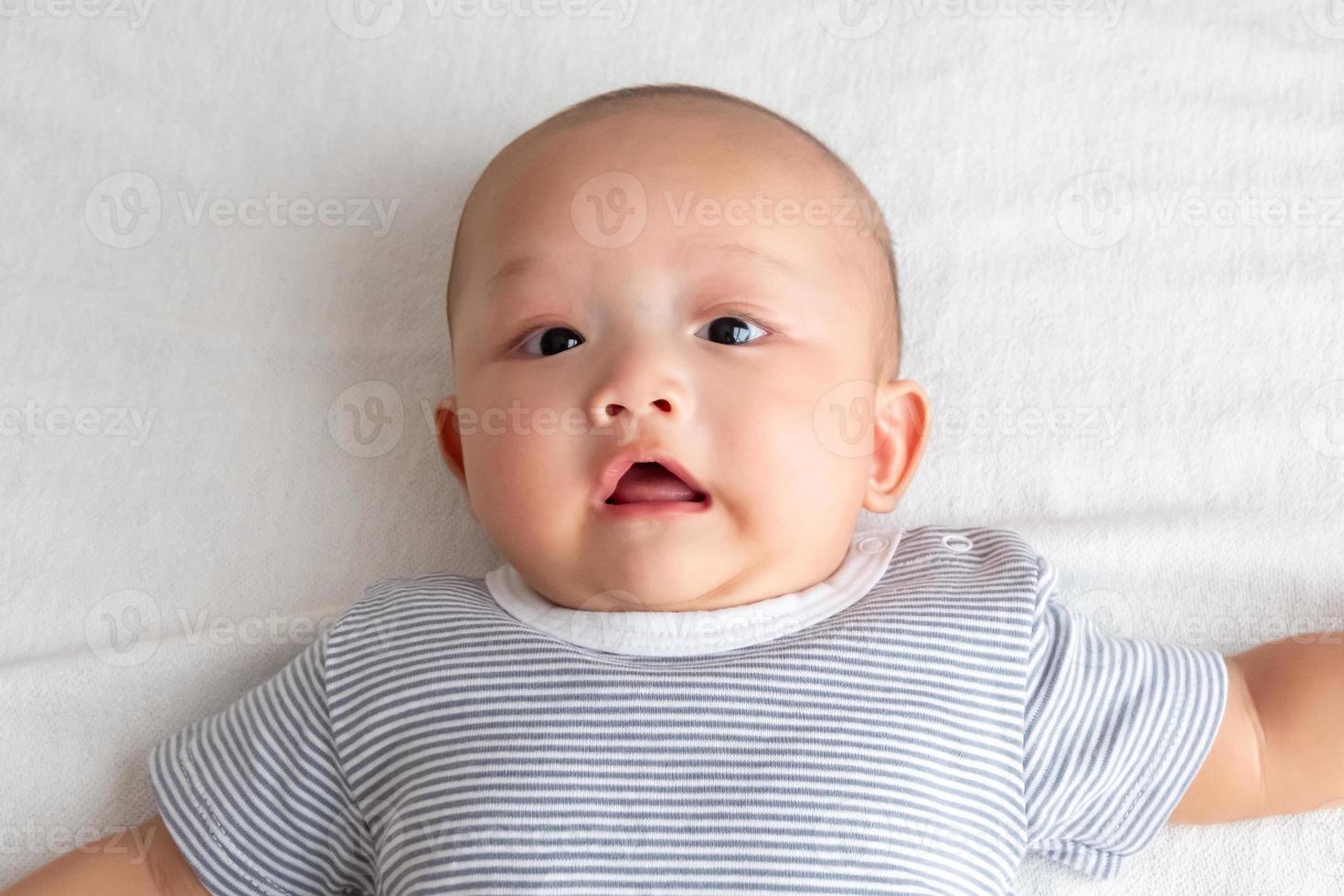 um bebê em uma camisa listrada está chocado no tapete branco. foto