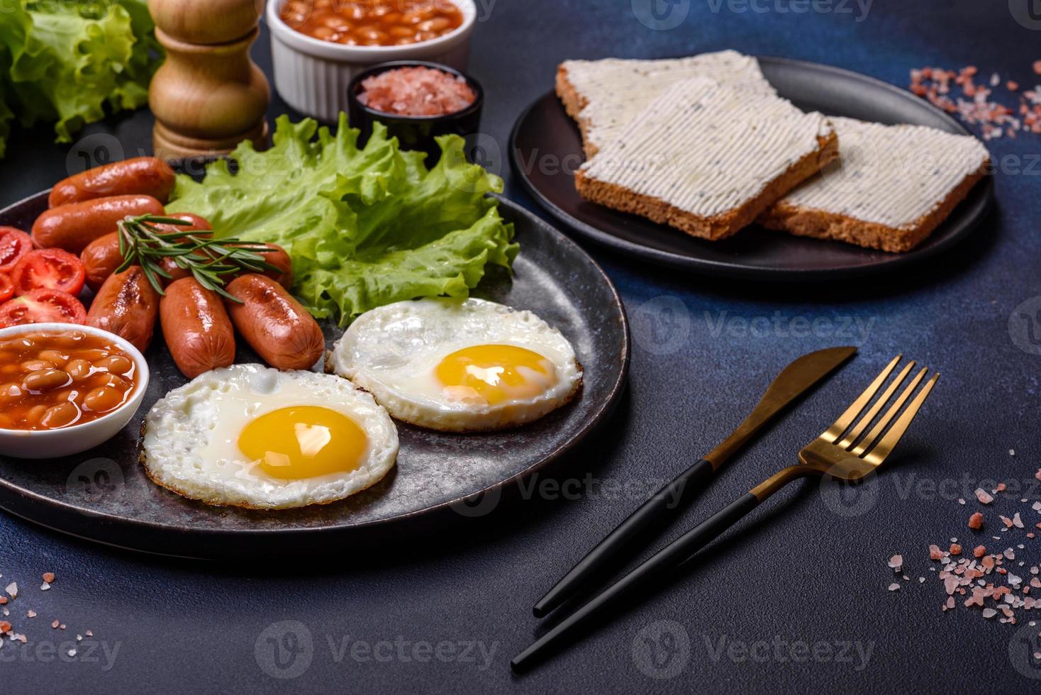 café da manhã inglês tradicional com ovos, torradas, salsichas, feijão, especiarias e ervas em um prato de cerâmica cinza foto