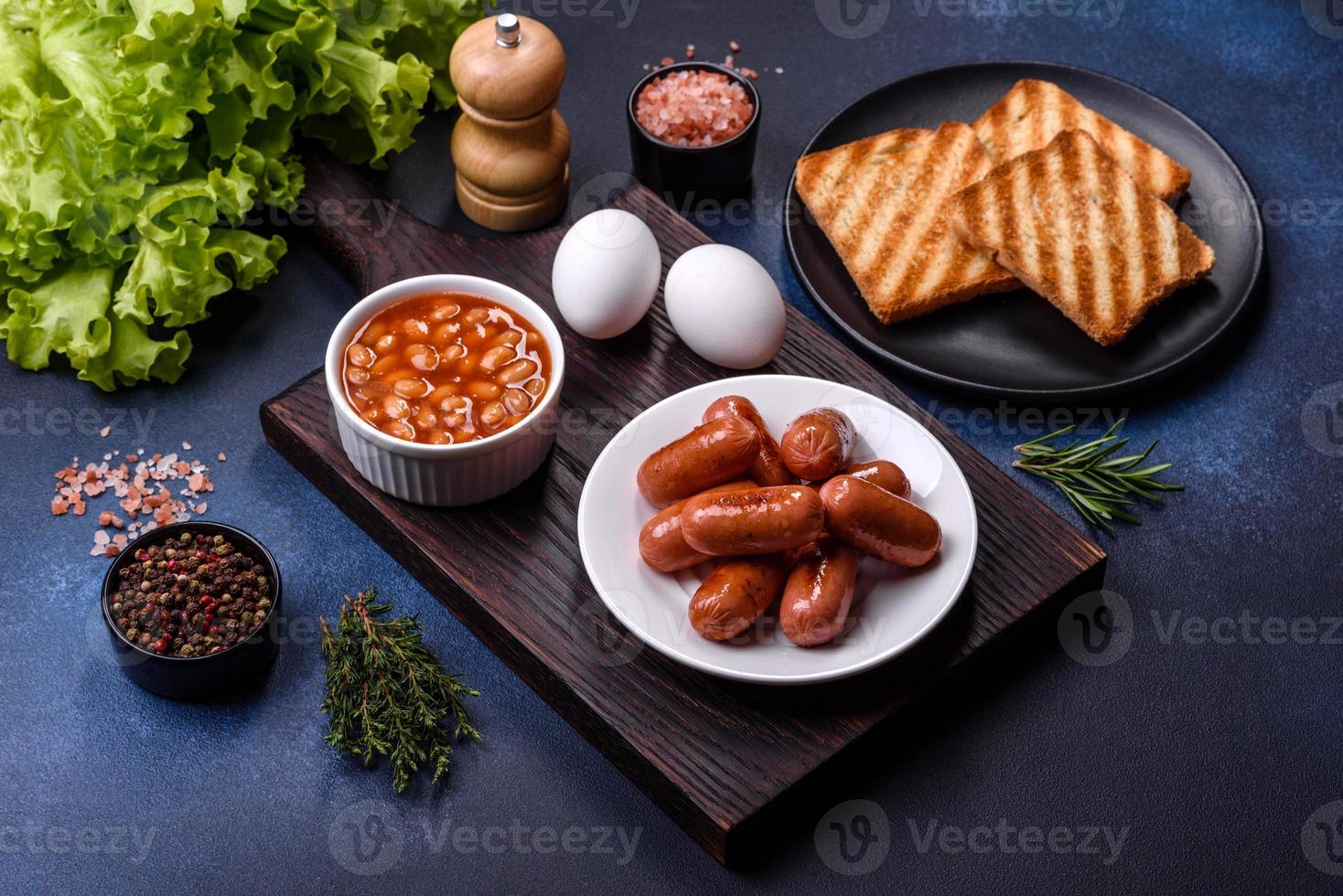 café da manhã inglês tradicional com ovos, torradas, salsichas, feijão, especiarias e ervas em um prato de cerâmica cinza foto