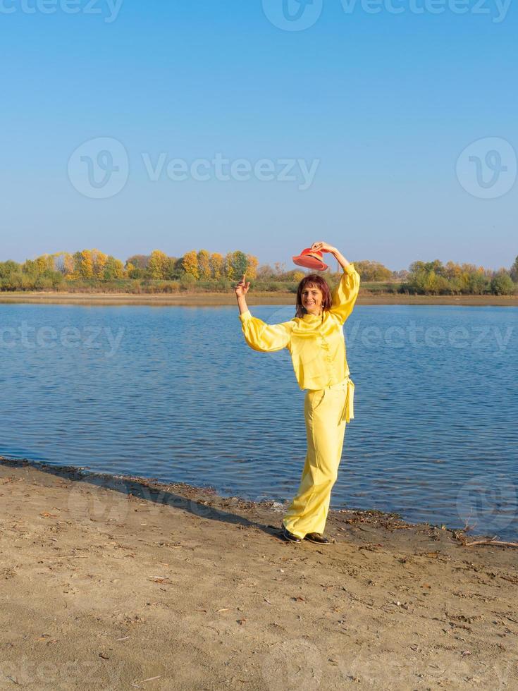 mulher com roupas amarelas com chapéu vermelho posando à beira do lago no outono foto