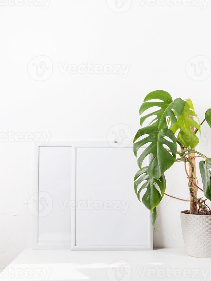 maquete de moldura branca com flores monstera em uma mesa branca foto