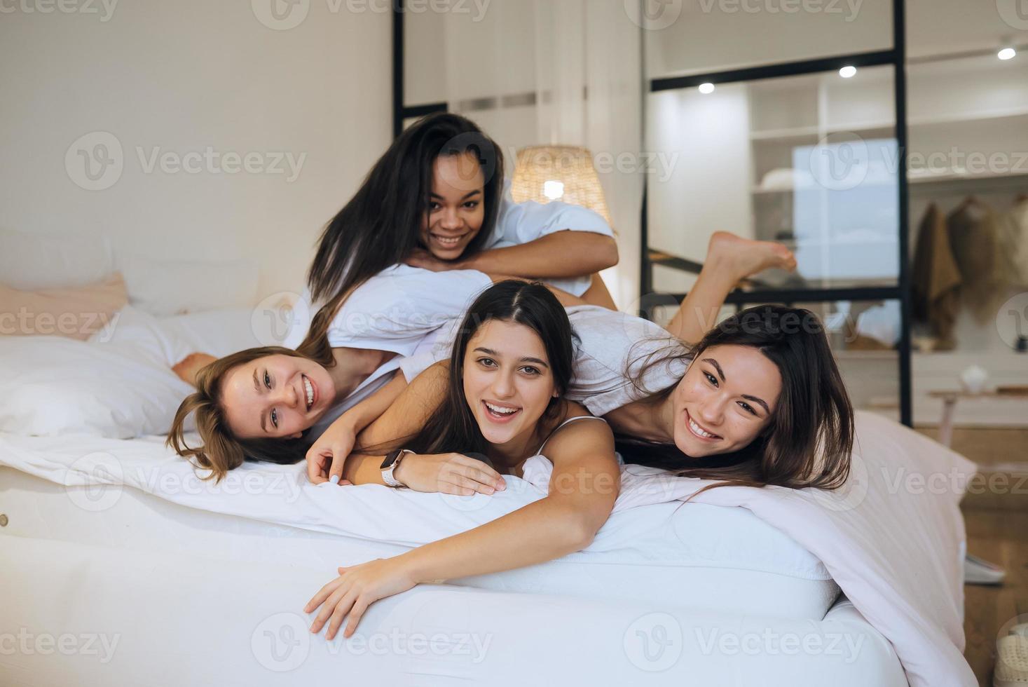 meninas positivas mulheres amigas dentro de casa na cama na festa de despedida em casa. foto